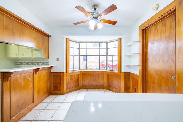 kitchen with light tile patterned floors, brown cabinetry, decorative backsplash, wainscoting, and light countertops