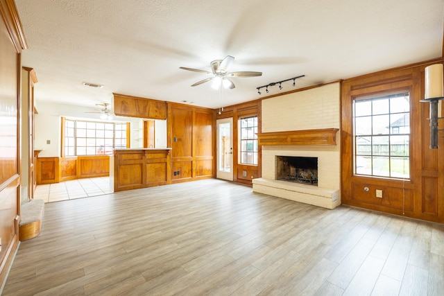 unfurnished living room with ceiling fan, a textured ceiling, wood walls, light wood-type flooring, and a brick fireplace