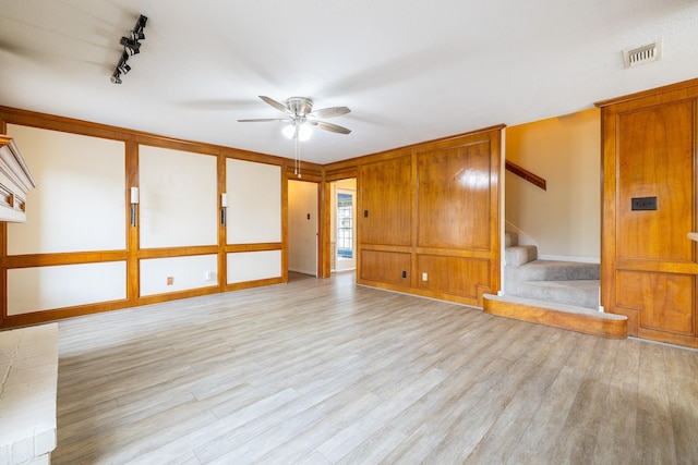 unfurnished living room with ceiling fan, wood finished floors, visible vents, stairs, and rail lighting