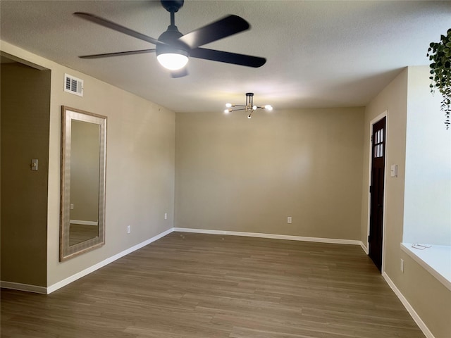 unfurnished room with a textured ceiling, wood finished floors, visible vents, and baseboards