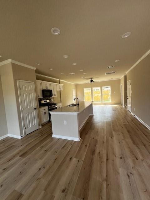 kitchen with ornamental molding, open floor plan, stainless steel range with gas stovetop, a sink, and black microwave