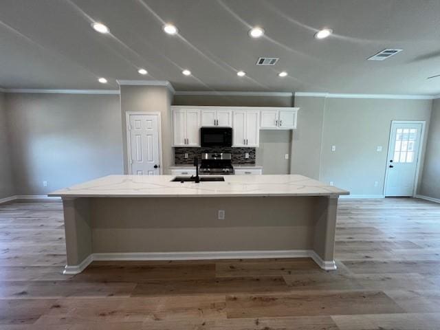 kitchen featuring black microwave, a sink, visible vents, white cabinets, and a large island with sink