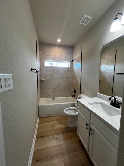 bathroom with toilet, wood finished floors, vanity, visible vents, and  shower combination