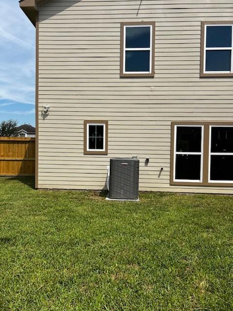 back of house featuring central air condition unit, fence, and a lawn