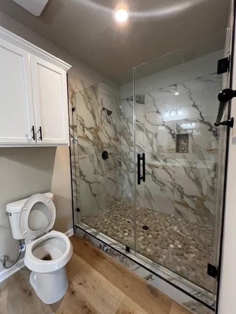 full bathroom with a marble finish shower, wood finished floors, toilet, and baseboards