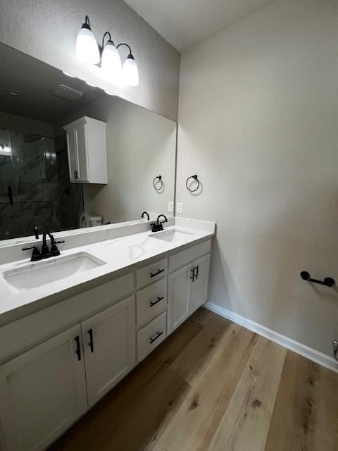 full bath with a stall shower, double vanity, a sink, and wood finished floors