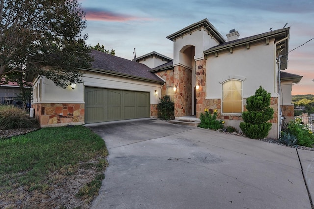 mediterranean / spanish-style house with a garage, stone siding, concrete driveway, and stucco siding