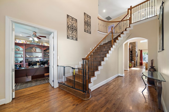 staircase featuring arched walkways, a high ceiling, ceiling fan, wood finished floors, and baseboards