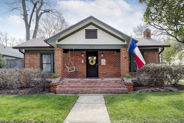 bungalow-style home with a shingled roof, a front yard, brick siding, and a chimney