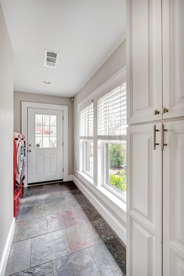 doorway with visible vents, washing machine and clothes dryer, stone tile flooring, and baseboards