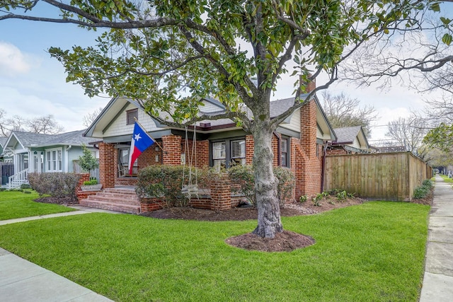 view of front of property with brick siding, fence, roof with shingles, a front lawn, and a chimney