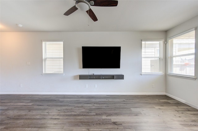 unfurnished living room with ceiling fan, baseboards, and wood finished floors