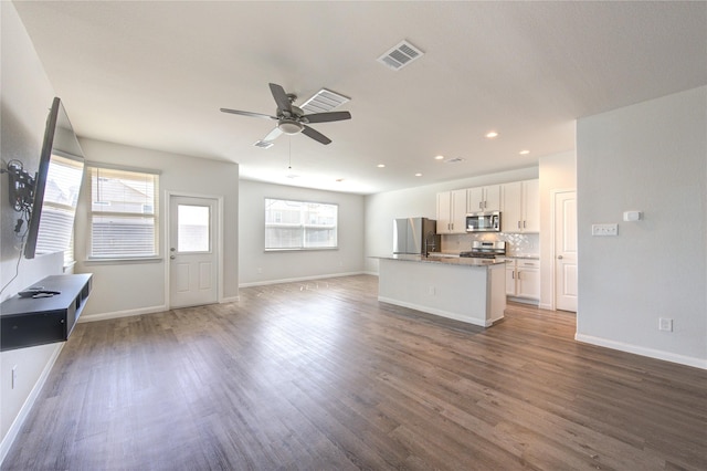 kitchen with visible vents, an island with sink, appliances with stainless steel finishes, open floor plan, and white cabinetry