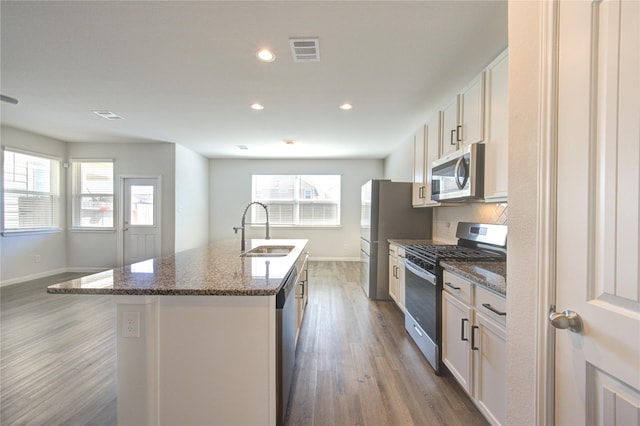 kitchen with a center island with sink, visible vents, appliances with stainless steel finishes, wood finished floors, and a sink