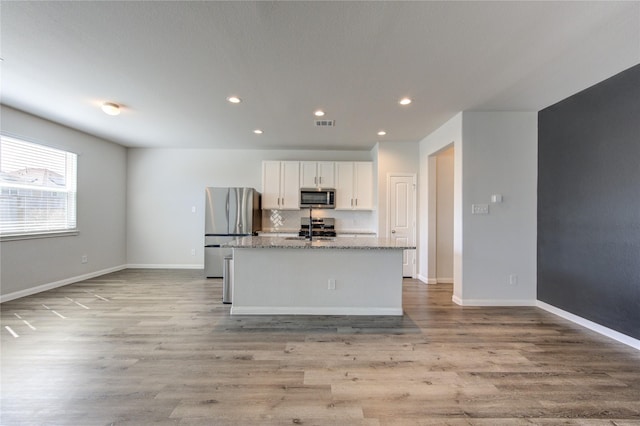 kitchen with a center island with sink, light wood-style flooring, appliances with stainless steel finishes, white cabinets, and baseboards