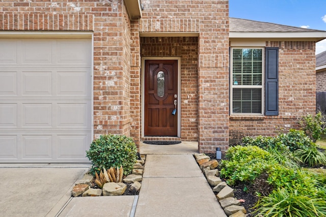 doorway to property featuring a shingled roof, brick siding, and an attached garage