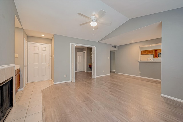 unfurnished living room with lofted ceiling, a fireplace, light wood-style flooring, and baseboards