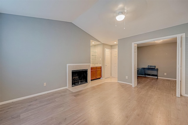 unfurnished living room featuring a ceiling fan, baseboards, vaulted ceiling, light wood-style floors, and a tiled fireplace