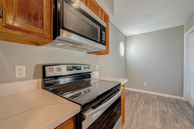 kitchen with stainless steel appliances, baseboards, light countertops, light wood finished floors, and brown cabinetry