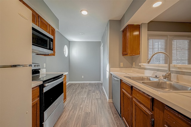 kitchen with appliances with stainless steel finishes, brown cabinets, a sink, and light countertops