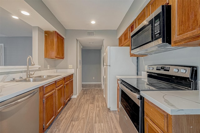 kitchen with light wood finished floors, stainless steel appliances, visible vents, brown cabinetry, and a sink