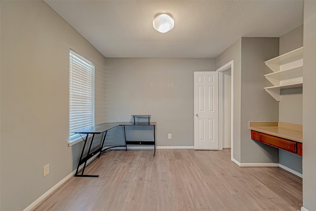 unfurnished office featuring baseboards, a textured ceiling, and light wood finished floors