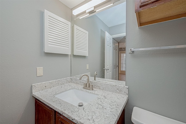 bathroom featuring a textured wall, vanity, and toilet