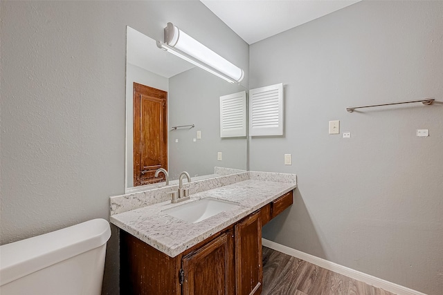 bathroom with baseboards, vanity, toilet, and wood finished floors