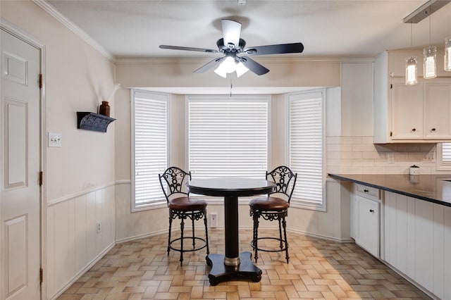 dining space with ceiling fan, ornamental molding, and wainscoting