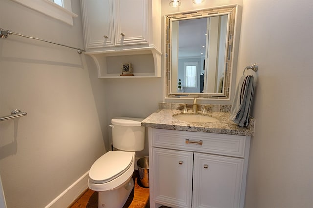 half bathroom featuring vanity, toilet, and baseboards