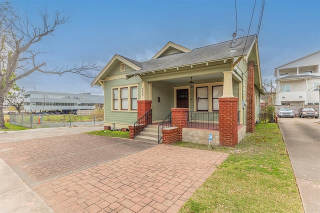 bungalow-style house with a porch, decorative driveway, a shingled roof, and fence