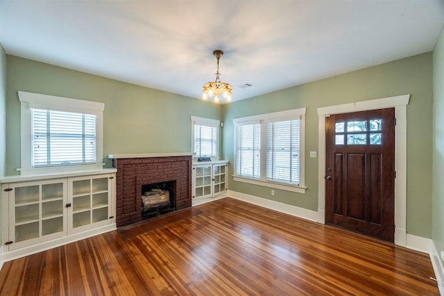 foyer featuring dark wood-type flooring, a fireplace, baseboards, and an inviting chandelier