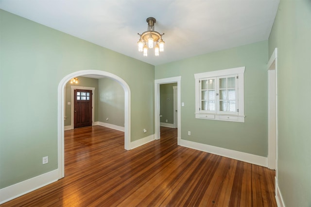 empty room with arched walkways, baseboards, and wood finished floors