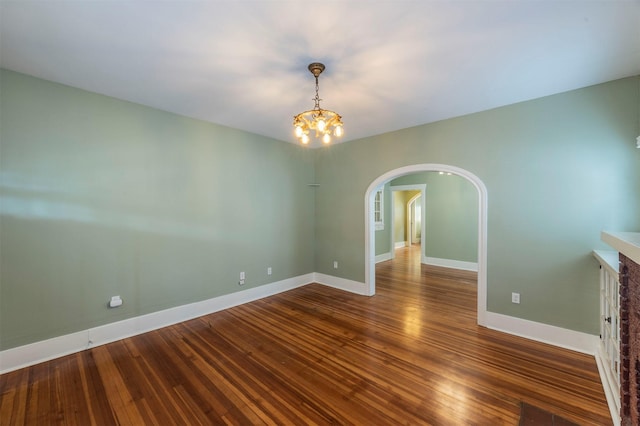 unfurnished room with arched walkways, an inviting chandelier, hardwood / wood-style flooring, and baseboards