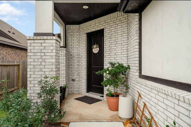 view of exterior entry featuring brick siding and fence