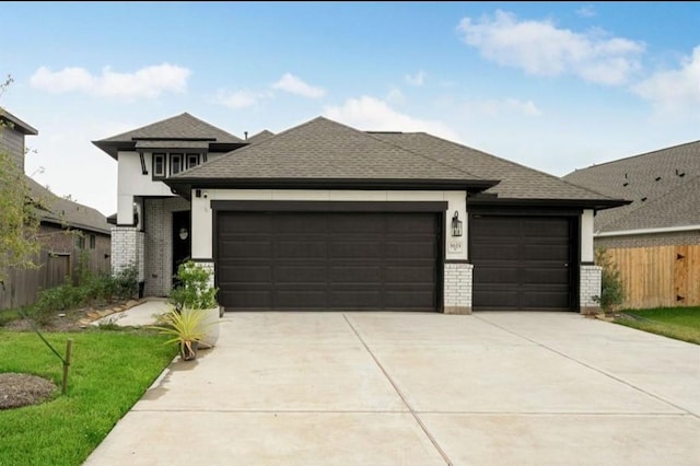 prairie-style home with driveway, brick siding, an attached garage, and fence