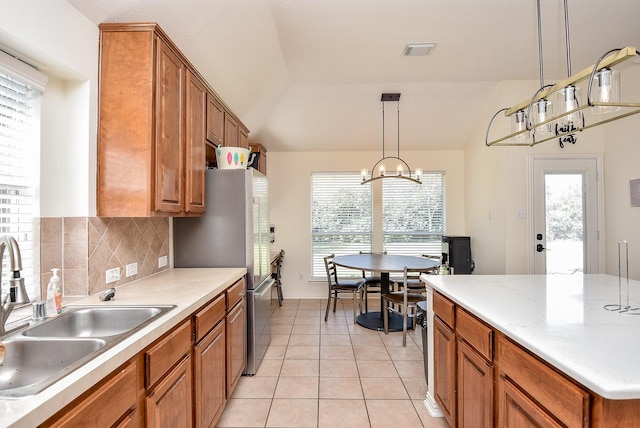 kitchen featuring light tile patterned floors, a sink, brown cabinets, tasteful backsplash, and decorative light fixtures