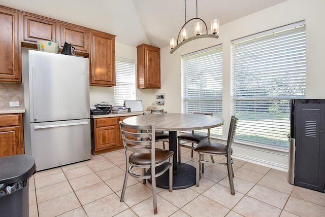 kitchen featuring light tile patterned floors, brown cabinetry, lofted ceiling, and freestanding refrigerator