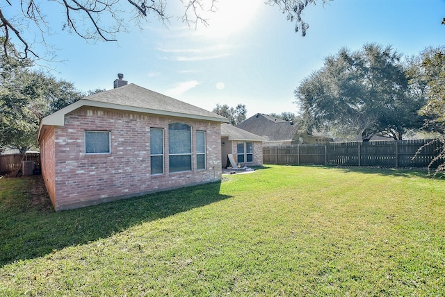 back of property featuring brick siding, a lawn, a chimney, and a fenced backyard