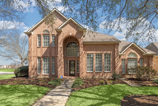 traditional-style home featuring a shingled roof, a front lawn, and brick siding