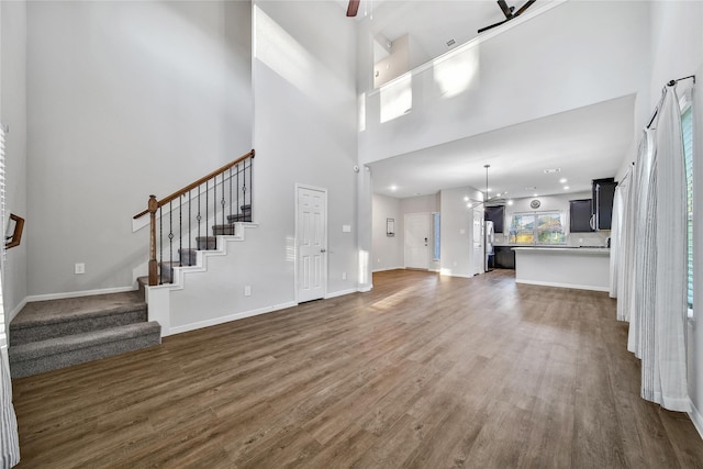 unfurnished living room featuring a towering ceiling, stairs, baseboards, and dark wood-style flooring