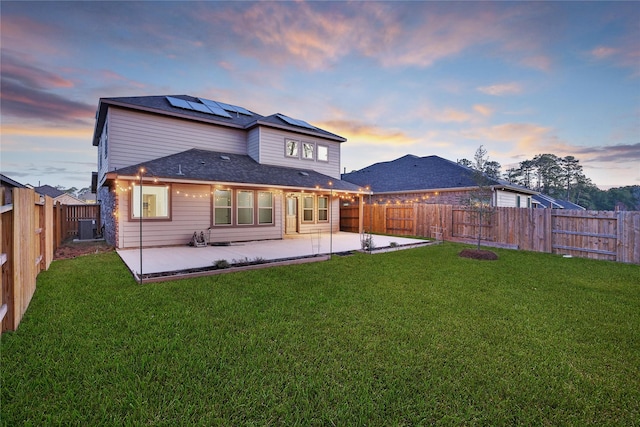 back of house at dusk with roof mounted solar panels, a patio area, a lawn, and a fenced backyard