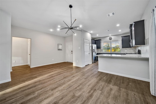 kitchen with a peninsula, visible vents, open floor plan, stainless steel refrigerator with ice dispenser, and decorative backsplash