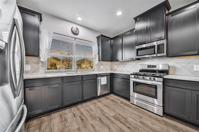 kitchen featuring light stone counters, light wood-style flooring, stainless steel appliances, a sink, and decorative backsplash