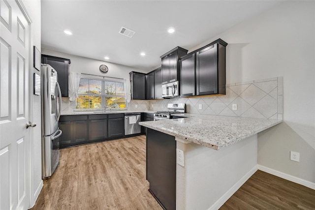 kitchen with stainless steel appliances, a peninsula, visible vents, light wood-type flooring, and decorative backsplash