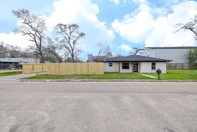 view of front of home featuring brick siding, roof with shingles, a front yard, and fence