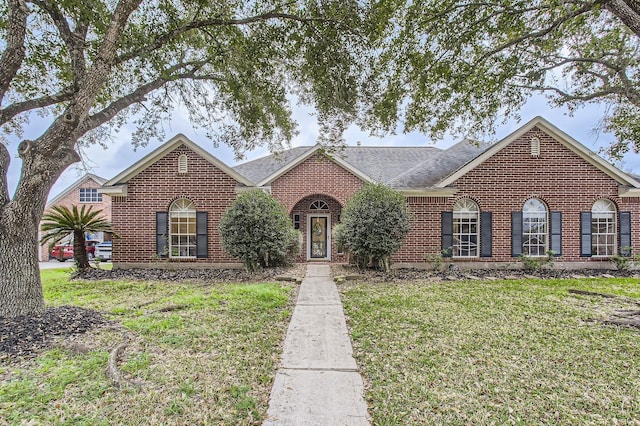 view of front facade featuring brick siding, roof with shingles, and a front yard