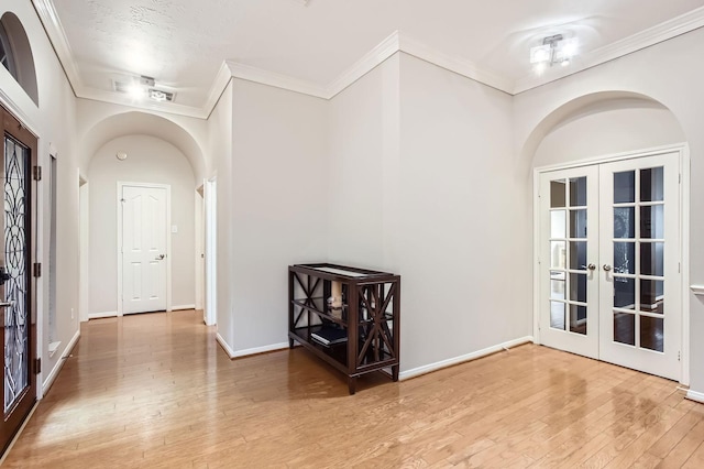 foyer featuring arched walkways, french doors, ornamental molding, baseboards, and hardwood / wood-style flooring