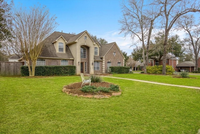 view of front of house featuring brick siding, roof with shingles, a front yard, and fence