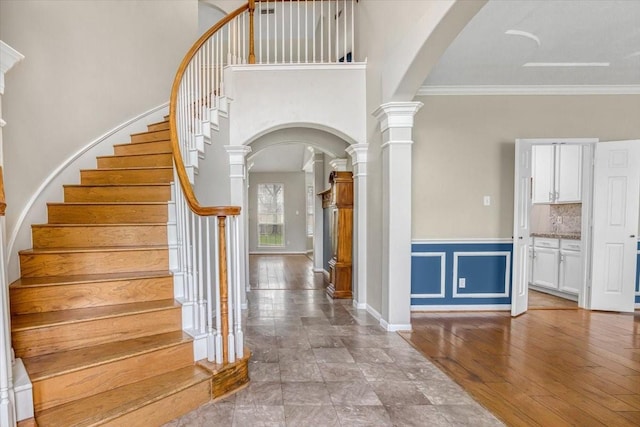 entryway with arched walkways, crown molding, wood-type flooring, and ornate columns